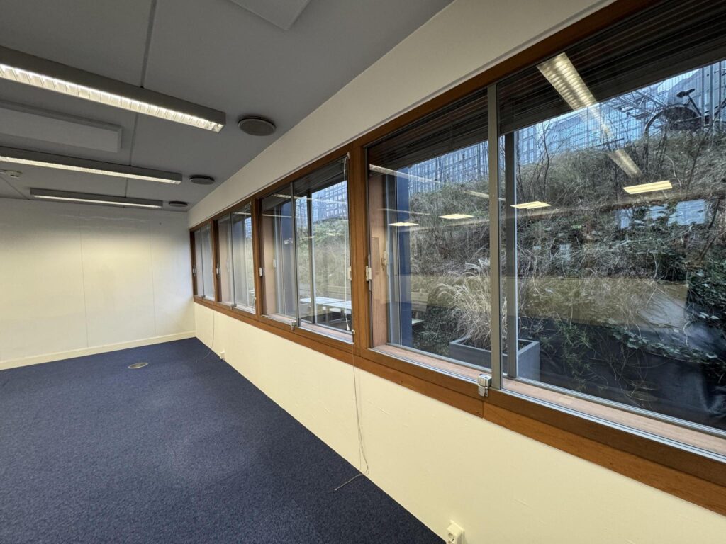Empty office space with blue carpet and large windows overlooking De Ruijterkade.